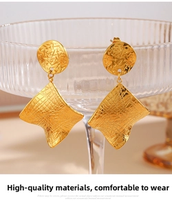 Detail of 18K gold geometric earrings with unique textured finish on a glass rim