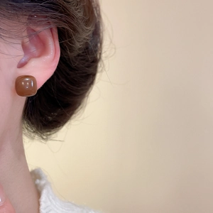 Close-up of caramel brown resin square stud earring worn on a model's ear