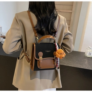 Detail of color-block backpack with metal buckle and plush bear pendant on model