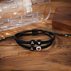 Pair of adjustable black woven heart and letter A bracelets on a warm wooden background
