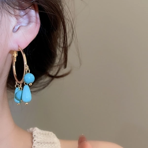 Close-up of bohemian gold hoop earrings with turquoise stone tassels worn by model