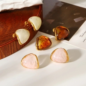 Three pairs of triangle resin earrings in white, amber, and pink on a wooden tray