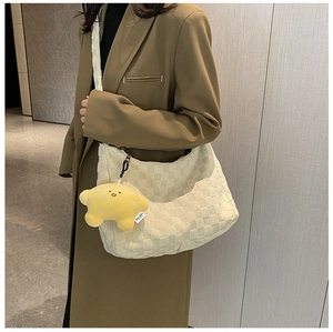 Detail of a large cream woven tote bag with a yellow star plush charm accessory