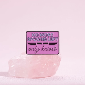 Vue macro d'un pin's émaillé rose avec texte NO MORE SPOONS LEFT et motif de poignard ciselé