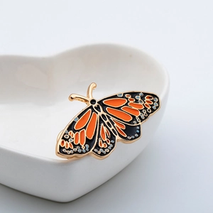 Primo piano di una spilla a farfalla in smalto su un vassoio di ceramica bianca a cuore