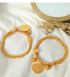 Close-up of dual gold beaded bracelets with engraved charms on elegant white silk