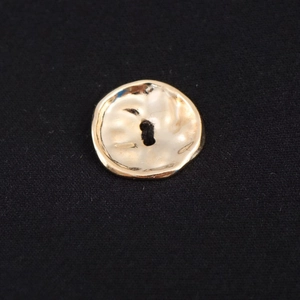 Macro shot of irregular hammered gold metal button on black knitted fabric texture