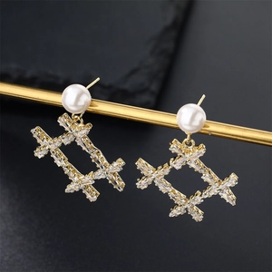 Elegant gold earrings with pearls and zircon geometric bow pendants on dark background