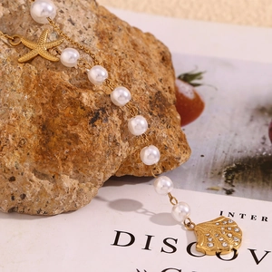 Close-up of 18K gold starfish and seashell pendants with pearls on a textured rock