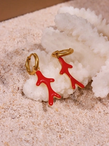 Detailed close-up of 18k gold plated coral red drop earrings on a white sand beach background