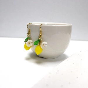 Close-up of yellow lemon and white flower charms hanging on a white ceramic bowl edge