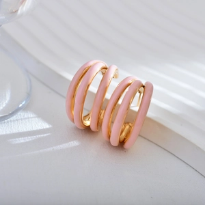 Close-up of pink enamel and gold-plated triple hoop earrings on a textured background