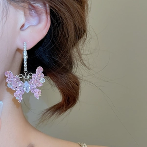 Dettaglio degli eleganti orecchini a farfalla con zirconi rosa indossati sul modello
