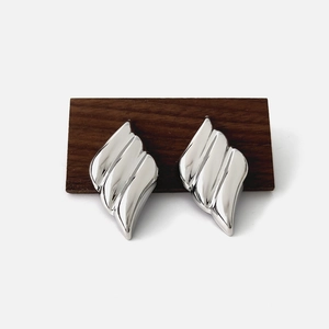 Detailed close-up of silver geometric diamond-shaped earrings with wavy texture on wood