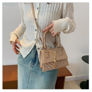 Detail of beige quilted handbag with gold V-logo, tassel charm, and top handle grip