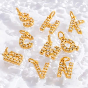Gold letter charms with cubic zirconia for DIY jewelry making on white textured surface