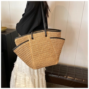 Close-up of a large capacity woven straw tote bag with black leather trim and shoulder straps