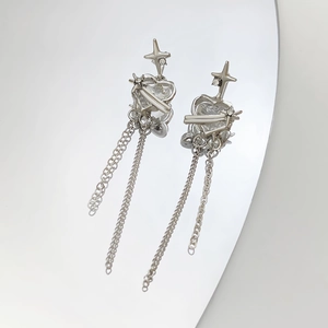 Macro detail of silver long tassel earrings with heart and star charms on mirror surface