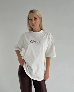 Détail du lettrage Cheers! imprimé sur un T-shirt blanc en coton à col rond
