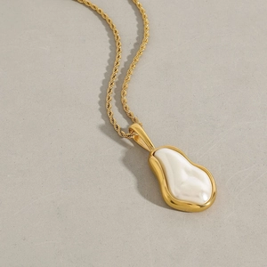 Detailed macro view of a gold twist chain necklace with a white baroque pearl pendant
