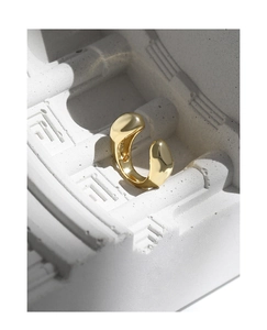 Dettaglio di un ear cuff dorato minimalista a forma di C con finitura lucida a specchio