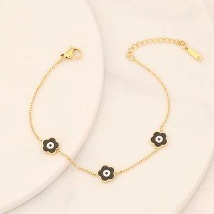 Macro detail of gold stainless steel bracelet featuring black flower charms and S-STEEL tag