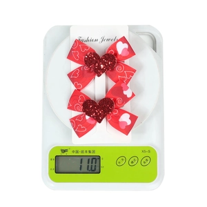 Detail shot of two red ribbon bow hair clips with glitter hearts on a digital scale