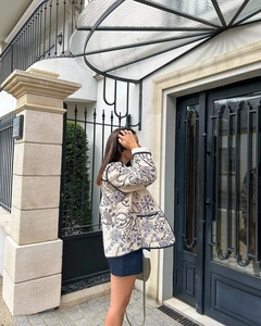 Close-up of beige quilted jacket with blue floral patterns and black contrast piping detail
