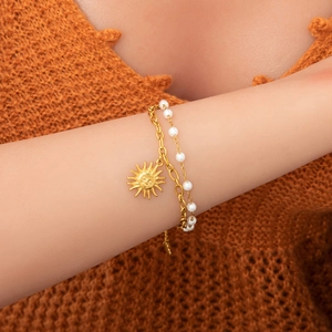 Détail du pendentif soleil plaqué or 18K et bracelet double couche en perles au poignet