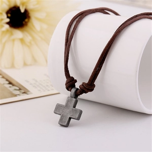 Detail of vintage silver cross pendant with double brown leather cord on soft background