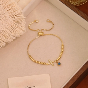 Dettaglio del bracciale con perline dorate, malocchio e croce in un vassoio di legno