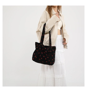 Detail of strawberry embroidery on black corduroy tote bag showing material texture