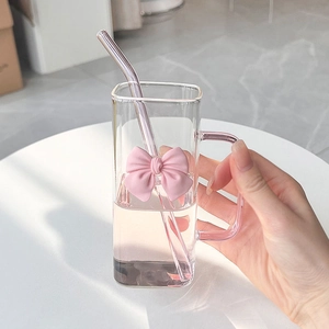 Square glass cup with pink 3D bow handle and glass straw on a marble table