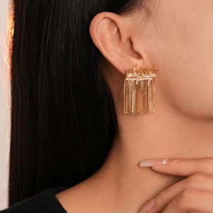 Close-up of gold dangling cross earrings with sparkling zircon tassels on female model