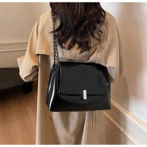 Close-up of black leather shoulder bag featuring silver chain strap and metal lock detail