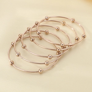 Detail of five rose gold stackable bracelets with polished beads on silk background