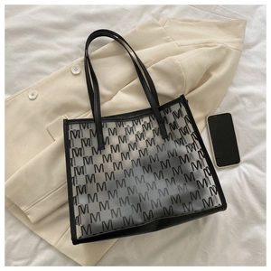 Macro detail of a large transparent tote bag with black M-pattern and leather trim