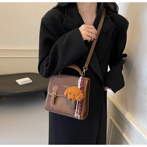 Detail of vintage brown shoulder bag with teddy charm on elegant black coat model