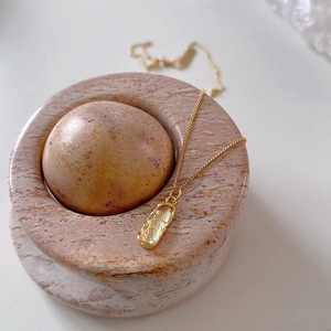 Macro detail of irregular gold rectangle pendant with vintage lava texture on pink marble