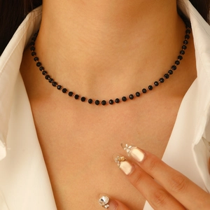 Detalle del collar de cuentas negras góticas con colgante de mariposa en camisa blanca
