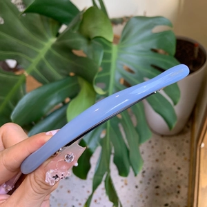 Handheld blue acetate hair clip with gold logo in a minimalist curved design