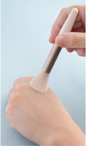 Close-up of portable makeup brush applying powder on hand with soft beige bristles