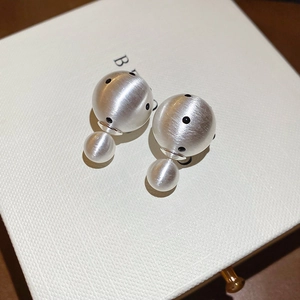 Macro detail of silver-finish double-ball earrings with matte brushed texture and black dots