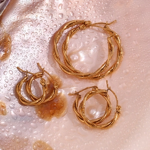 Detailed view of three sizes of gold-plated twisted hoop earrings on a wet pearl surface