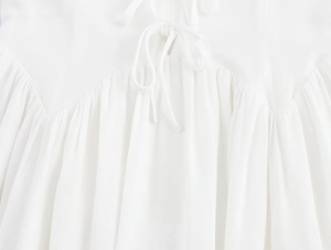 Close-up of a white dress featuring a delicate bow tie neckline and pleated details