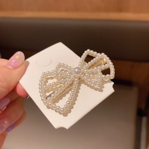 Detailed view of handmade pearl bow hair clip with gold metal base on display card