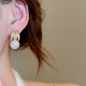 Close-up of golden M-shaped pearl earrings with sparkling cubic zirconia on a model