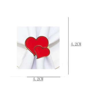Detail view of a 4.2cm gold napkin ring with red enamel double hearts on white fabric