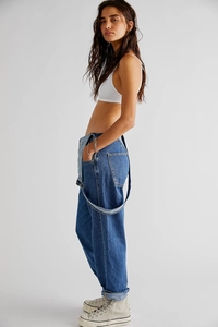 Detail view of washed denim overalls showing side cut, pocket, and vintage stitching