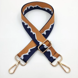 Detail of adjustable woven bag strap with brown and blue mountain pattern and gold hooks
